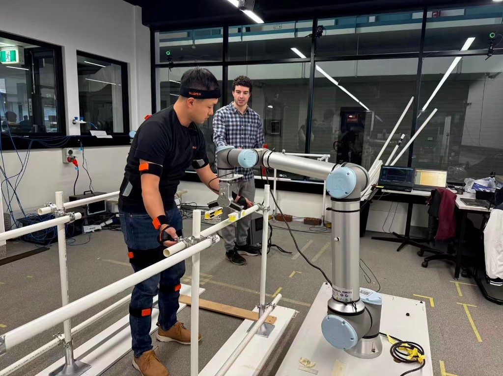 Researcher in motion capture gear collaborating with a UR10e robot on scaffold assembly